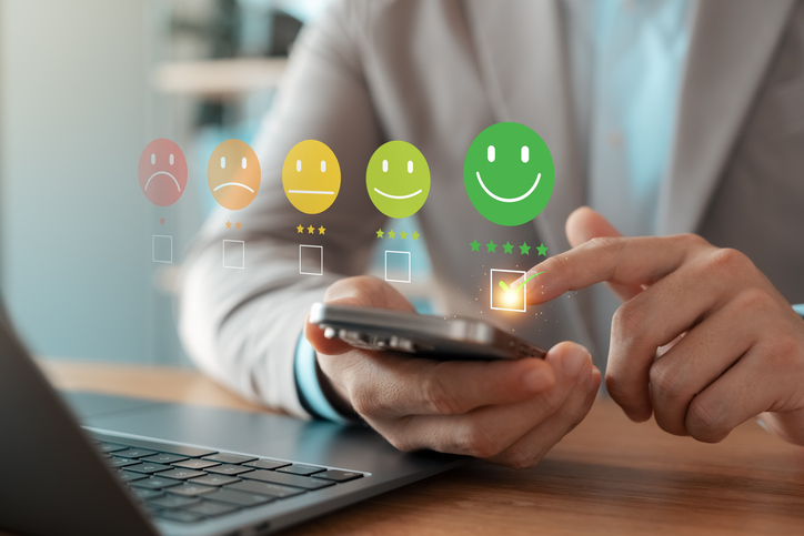 Teilnehmer beantwortet Online-Umfrage zur Forschung; über dem Handy erscheinen bunte Bewertungs-Smileys.
