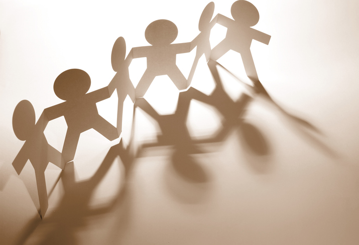 Papiermannchen halten sich an den Händen, licht kommt von hintenen, sodass die Figuren Schatten nach vorne werfen.