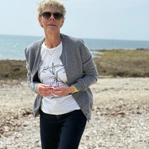 Andrea steht am Strand, das Meer ist im Hintergrund zu sehen.