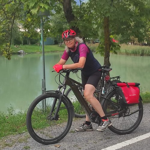 Rosemarie steht mit ihrem Rad an einer Straße, im Hintergrund ein Teich.