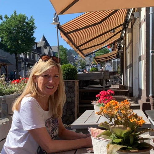 Brigitte sitzt in der Sonne am Holztisch im Außenbereich eines Restaurants.