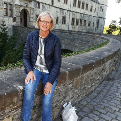 Christiane sitzt auf einer Mauer vor der Wewelsburg in Büren.