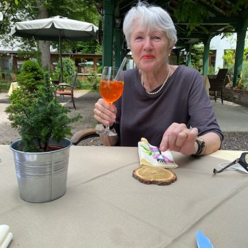 Ruth trinkt einen Aperol Spritz im Gartenbereich eines Restaurants.